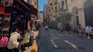 Rua com mesas ao ar livre, edifícios com varandas e céu claro.