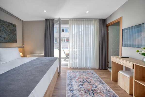 Ein modernes Hotelzimmer mit einem großen Bett, einem Schreibtisch, einem Fernseher und Blick auf die Stadt durch transparente Vorhänge.