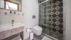 Ein Badezimmer mit Duschkabine aus Glas, einer weißen Toilette und einem Marmorwaschtisch.