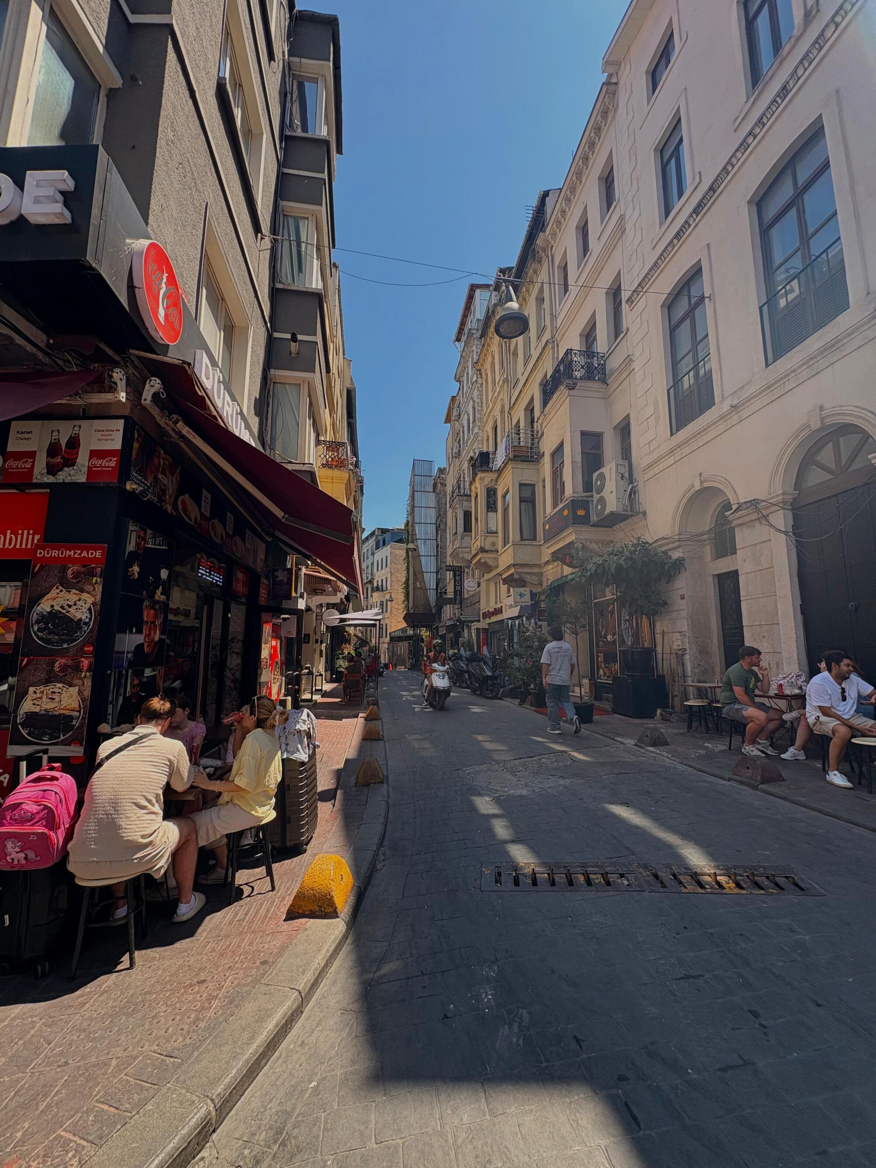 A street with buildings, outdoor seating, and a Coca-Cola sign.