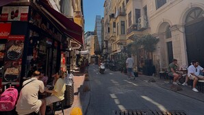 Rua com edifícios, mesas ao ar livre e um letreiro da Coca-Cola.