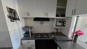 A compact kitchen with white cabinets, a gas stove, a microwave, and a sink. - Summer sands Air b n b (Durban)