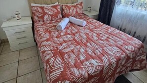 A bedroom with a bed, a nightstand, a dresser, a mirror, and a window with curtains. - Summer sands Air b n b (Durban)