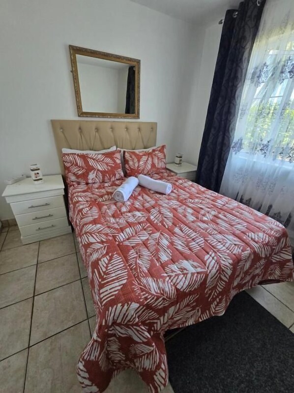 Un dormitorio con cama, mesita de noche, cómoda, espejo y ventana con cortinas.