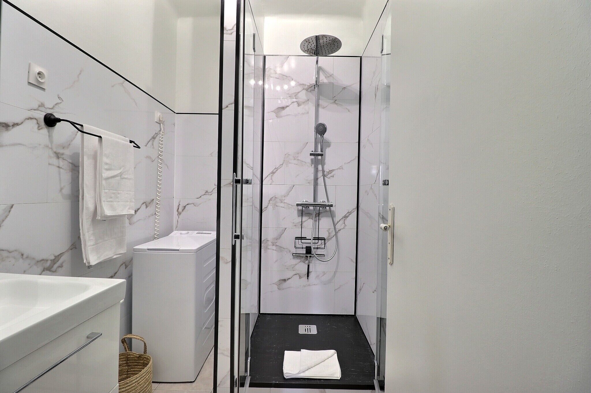 A modern bathroom with a glass-enclosed shower, a white marble wall, and a black floor.