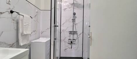 A modern bathroom with a glass-enclosed shower, a white marble wall, and a black floor.