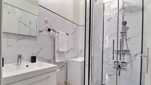 Un bagno moderno con rivestimento in marmo, cabina doccia in vetro, lavabo con rubinetto e porta asciugamani.