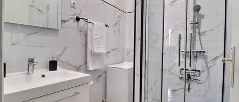 A modern bathroom with a marble backsplash, a glass shower enclosure, a sink with a faucet, and a towel rack.