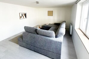 Ein modernes Wohnzimmer mit einer grauen Couch, einer Heizung und einem Fenster.