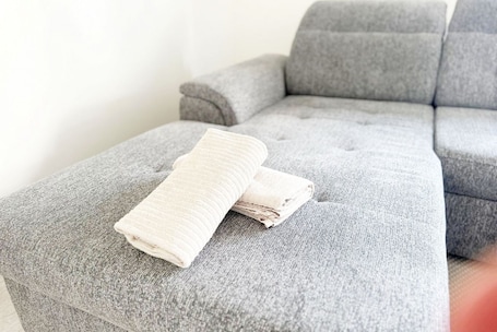 A grey upholstered sofa with a folded white towel on it.. Bright Modern Stay Near Downtown | High-Speed Wi-Fi & Comfort