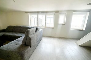 Ein Zimmer mit einer Eckcouch, großen Fenstern und einer Treppe.