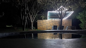 Ein Gebäude mit einer Steinfassade, ein Pool im Vordergrund und Sitzgelegenheiten im Freien bei Nacht.