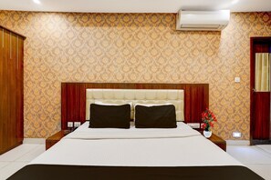 Een hotelkamer met een groot bed, een houten hoofdeinde, een rood gordijn en een airconditioner aan de muur.