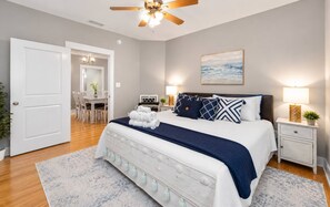 A bedroom with a bed, bedside tables, a ceiling fan, a painting, and a dining area with chairs and a table. - 5003 R3 Serene Beach Cottage in Gulf Shores 3BR 2 Bath, Sleeps 10 (Gulf Shores)