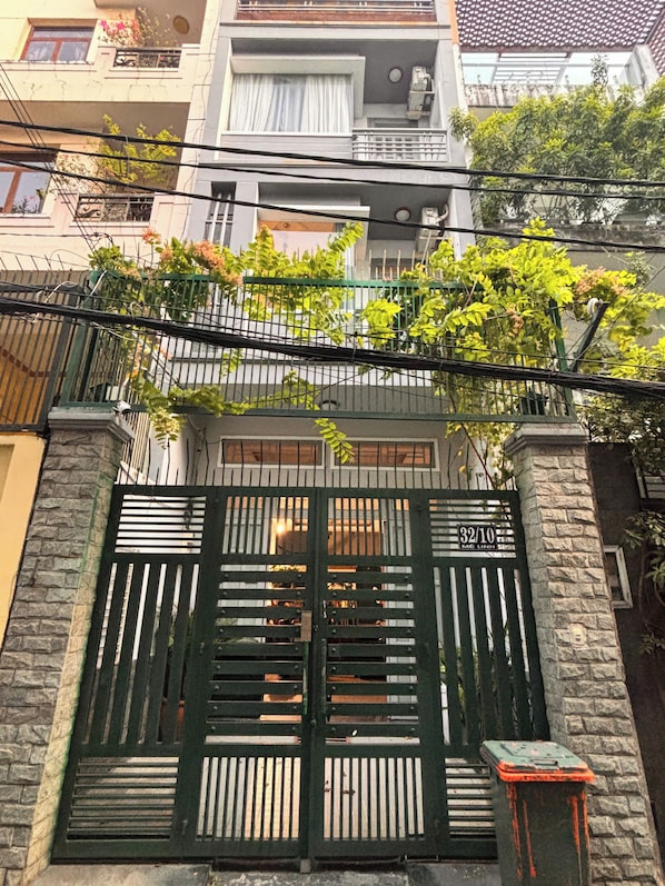 A gated entrance with a stone wall, a metal gate, and a small table with a box on it. - Darlington House Mê Linh (Thanh My Tay)