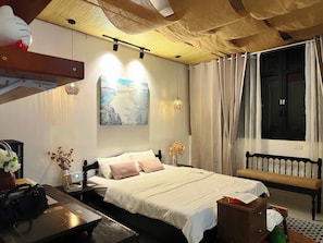 A bedroom with a bed, bedside table, lamp, artwork, and a window with curtains. - Darlington House Mê Linh (Thanh My Tay)