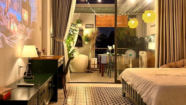 A modern hotel room with a bed, a desk, a chair, a small table, a fan, and a view of the outside. - Darlington House Mê Linh (Ho Chi Minh City)