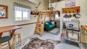 Een landelijke inrichting met een houten tafel, een ladder, een groene bank, een oude fornuis en gewei aan de muur.