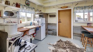 Een kleine keuken met een magnetron, broodrooster, koelkast en een houten tafel met stoelen.