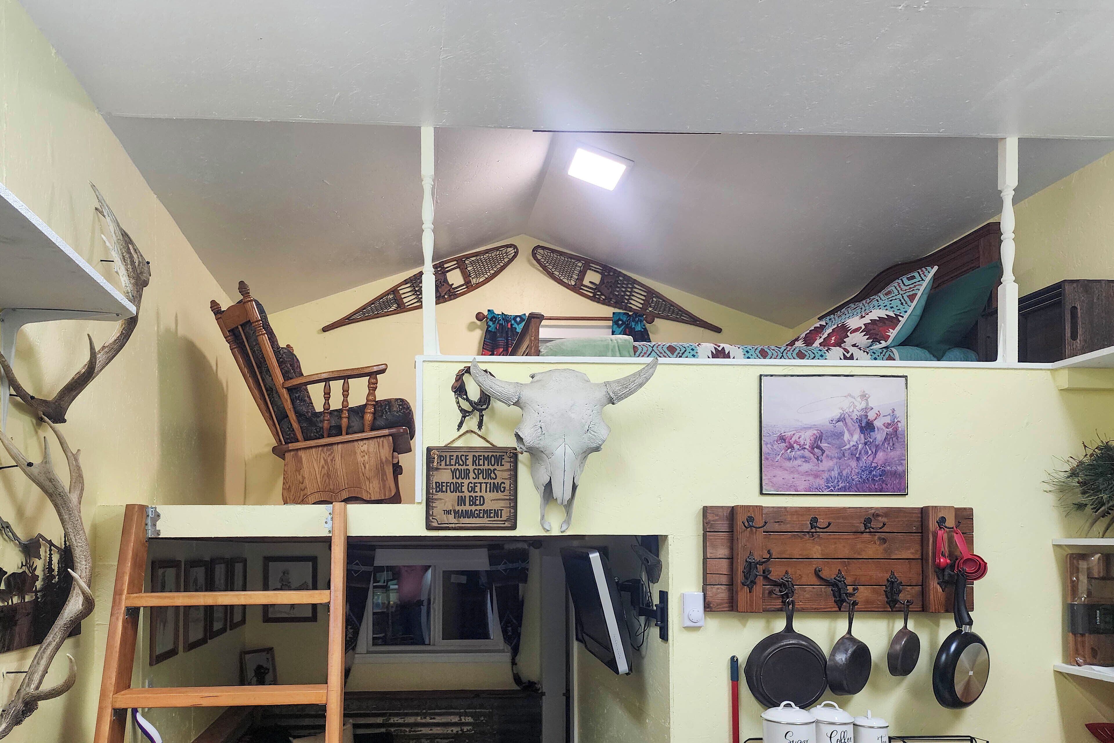 Ein Zimmer mit Hochlakenbett, einem aufgehängten Schädel, an der Wand befestigten Kochutensilien und einem Schild mit der Bitte, Sporne abzulegen.
