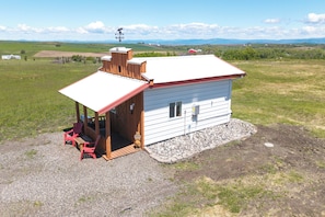 A small cabin with a porch, a red roof, and a gravel driveway.