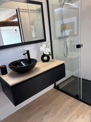 Ein modernes Badezimmer mit einem schwarzen Waschbecken, einer Holzauskleidung, einem Spiegel und einer Duschkabine aus Glas.