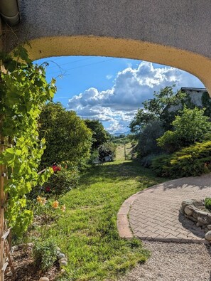A garden pathway under a bridge with greenery and a clear sky.