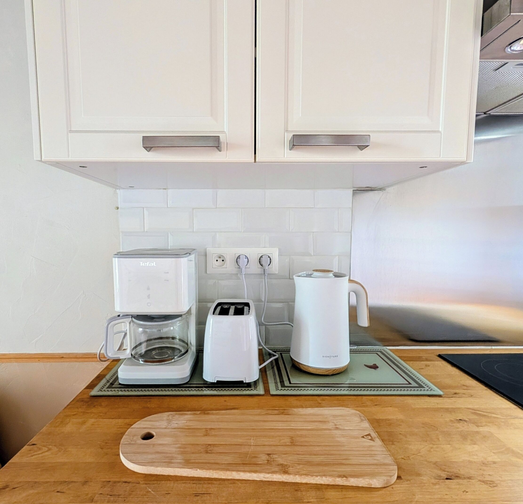Una cocina con alacenas blancas, una cafetera, un tostador y un hervidor sobre una encimera de madera.