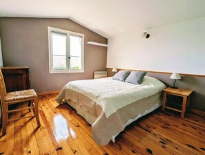 A bedroom with a bed, a chair, a nightstand, a lamp, a window, and a door.