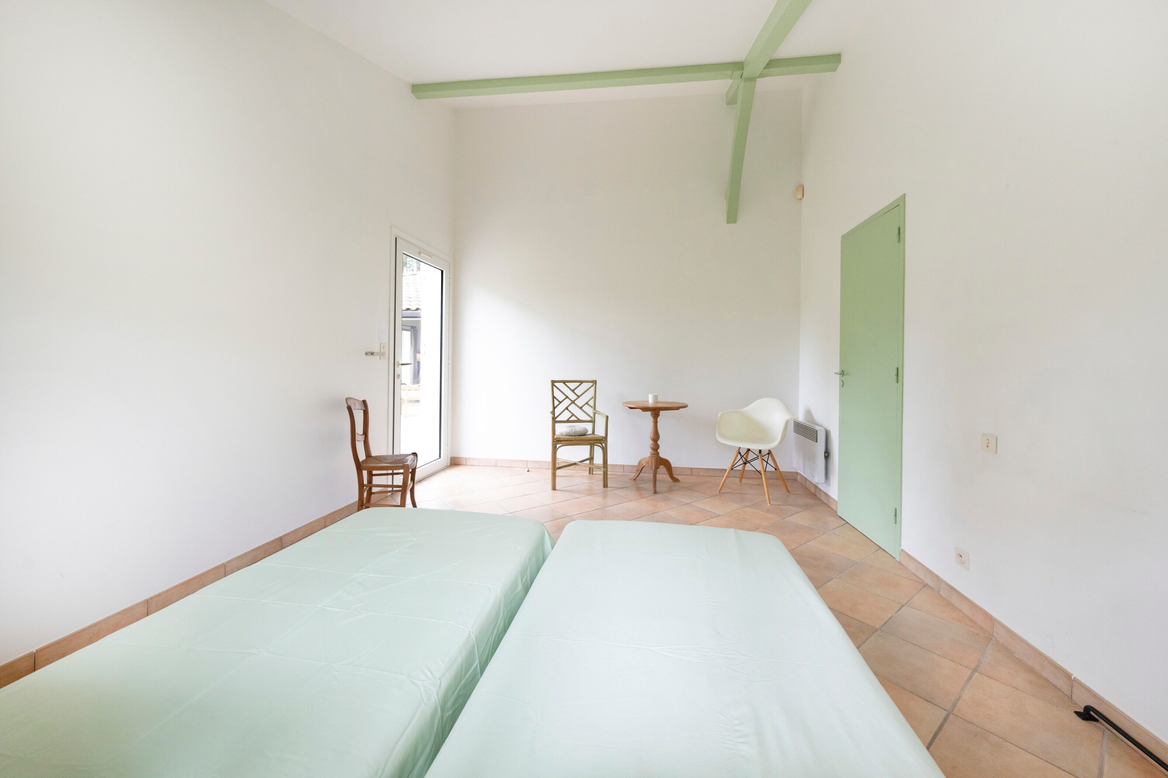 Une pièce avec deux lits, une chaise, une petite table et une porte.