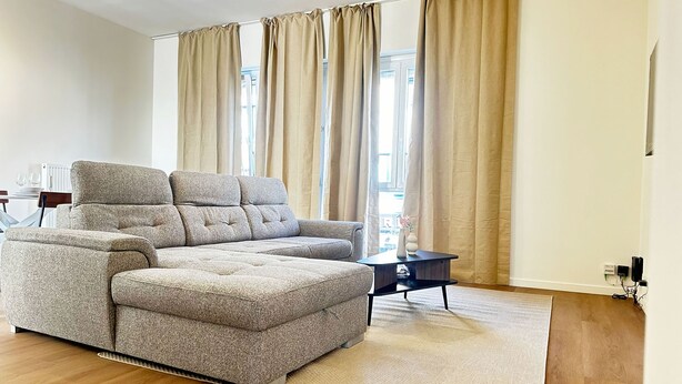 Una sala de estar moderna con un sofá modular, una mesita auxiliar y un amplio ventanal con cortinas.