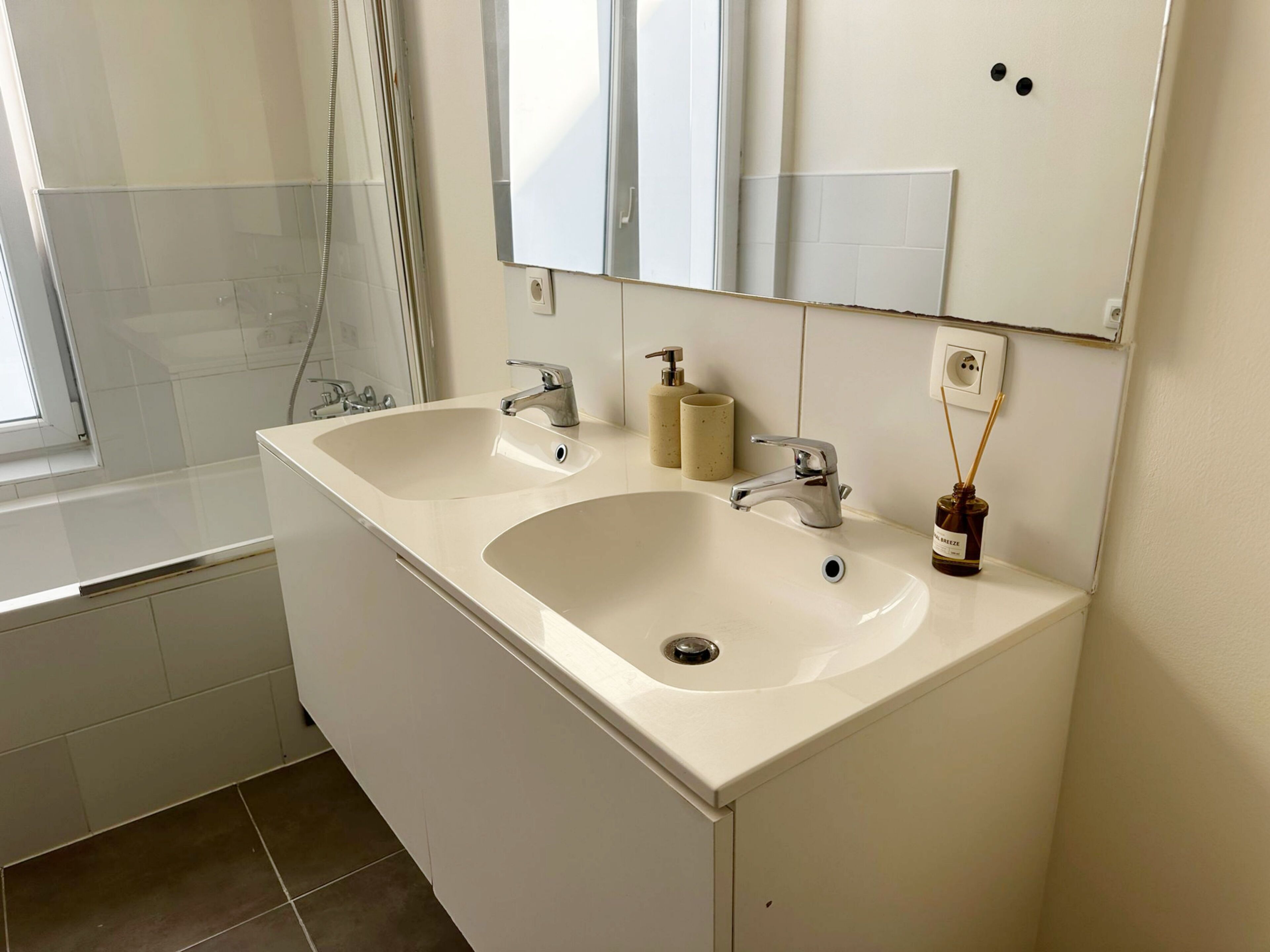A bathroom with two sinks, a mirror, a window, and a shower.