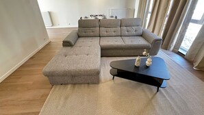 Una sala de estar moderna con un sofá seccional, una pequeña mesa de centro y un comedor al fondo.