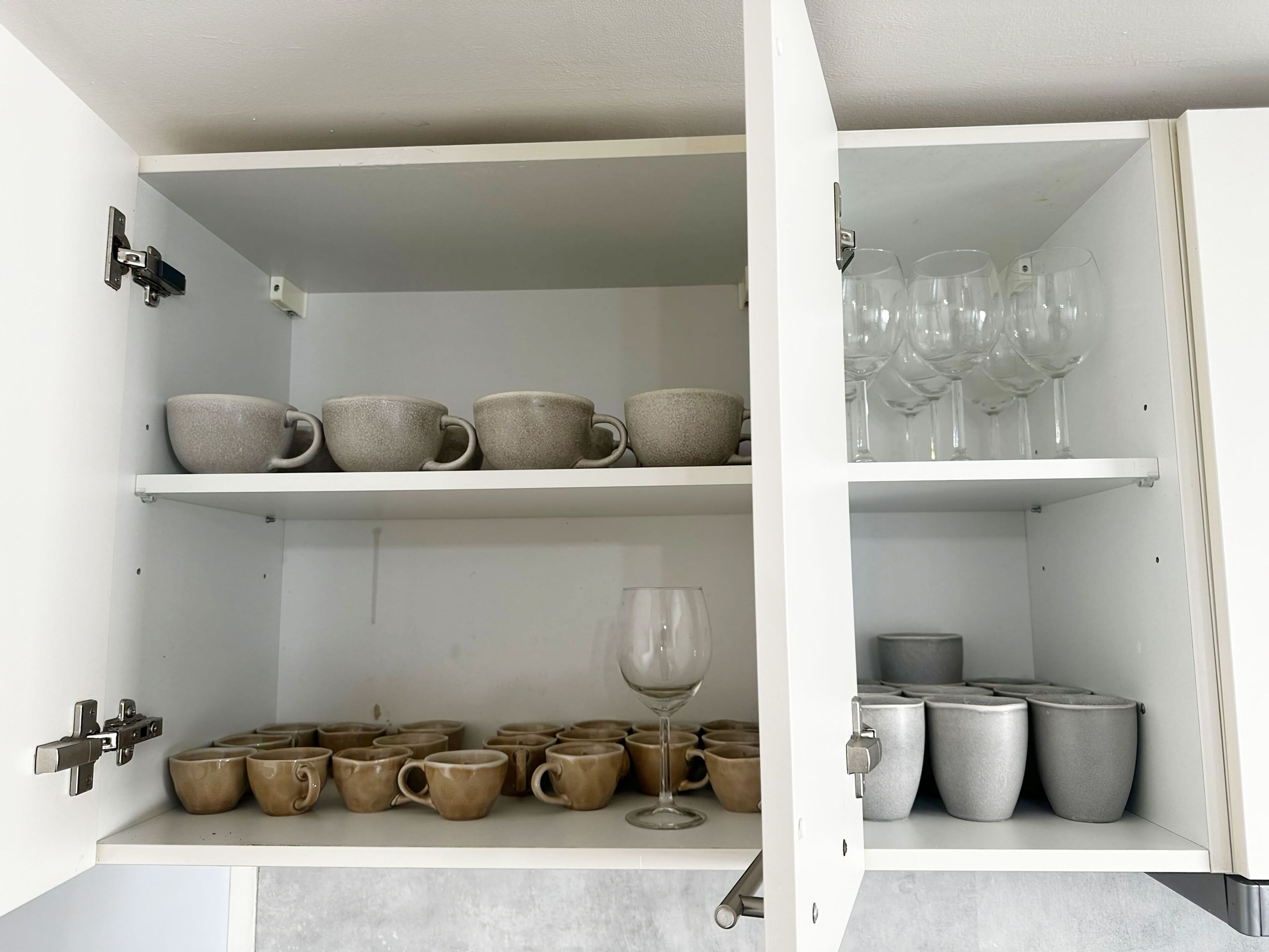 Un mobile bianco con ripiani che contengono tazze in ceramica, un bicchiere da vino e bicchieri trasparenti.