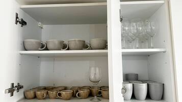 Un mobile bianco con ripiani che contengono tazze in ceramica, un bicchiere da vino e bicchieri trasparenti.
