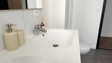 Un baño con lavamanos blanco, un espejo, un inodoro y una zona de ducha.