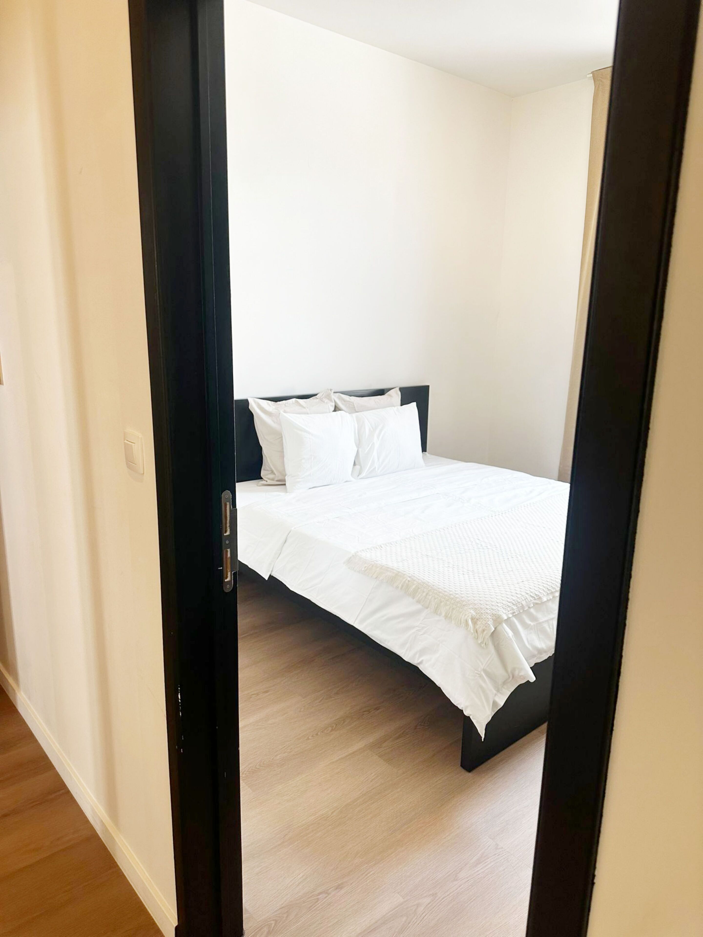 Ein Schlafzimmer mit einem Bett, weißer Bettwäsche, einem dunklen Kopfteil und Holzboden.