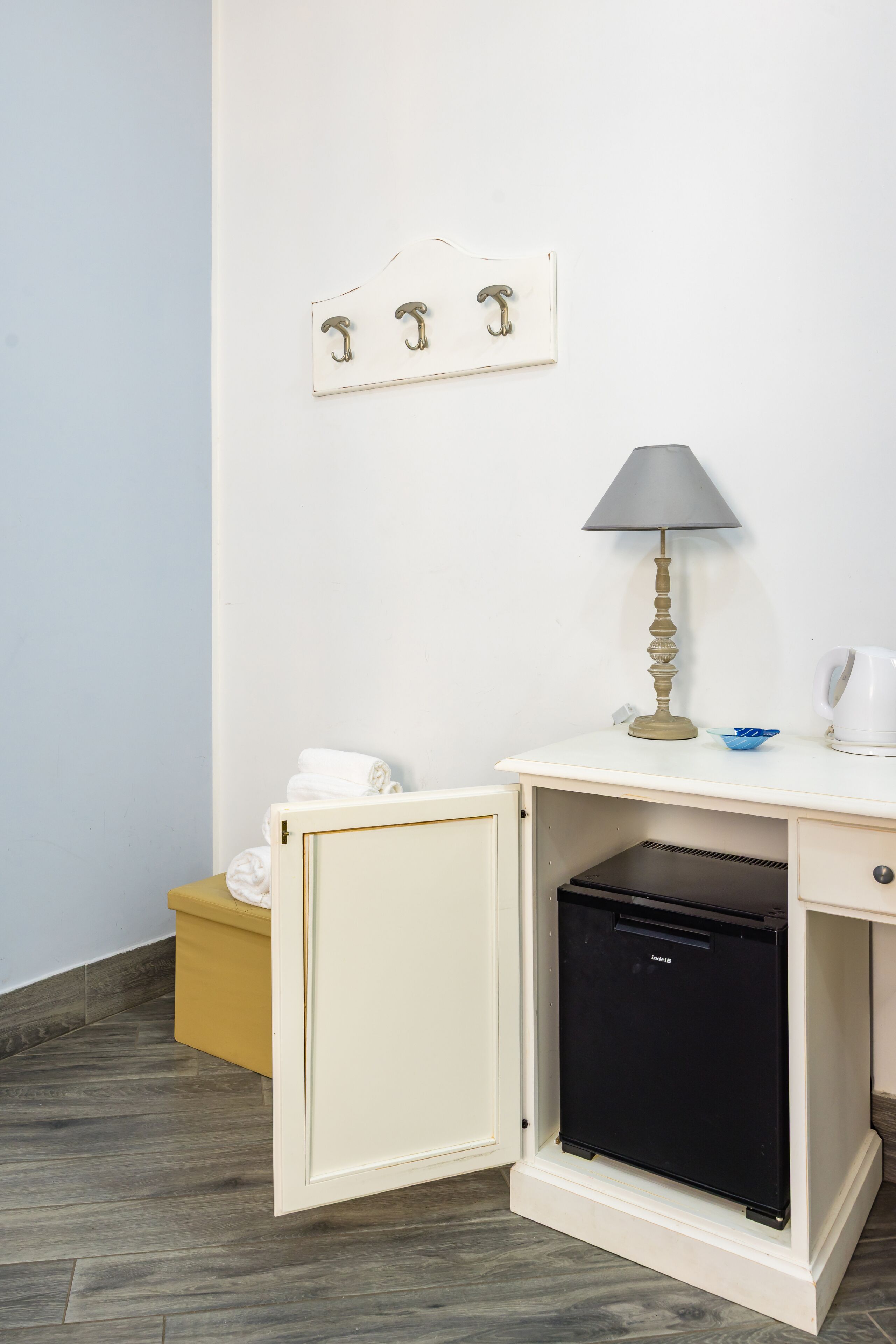 A compact kitchenette with a small refrigerator, a lamp, and a towel rack.