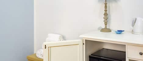A compact kitchenette with a small refrigerator, a lamp, and a towel rack.