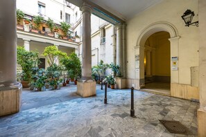 A courtyard with marble flooring, columns, potted plants, and a sign indicating hotel amenities. - Agorà Borsa (Naples)