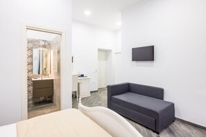 A hotel room with a bed, a desk, a chair, a TV, and a bathroom with a mirror and towel rack. - Agorà Borsa (Naples)