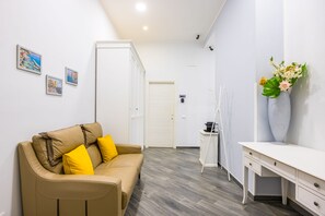 A room with a beige sofa, a white desk, and a vase with flowers. - Agorà Borsa (Naples)