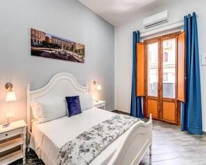 A bedroom with a bed, a nightstand, a wall-mounted lamp, a window with curtains, and an air conditioning unit. - Agorà Borsa (Naples)