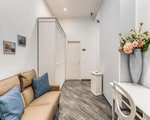 A room with a beige sofa, a small white table, a white wardrobe, and a white door. - Agorà Borsa (Naples)