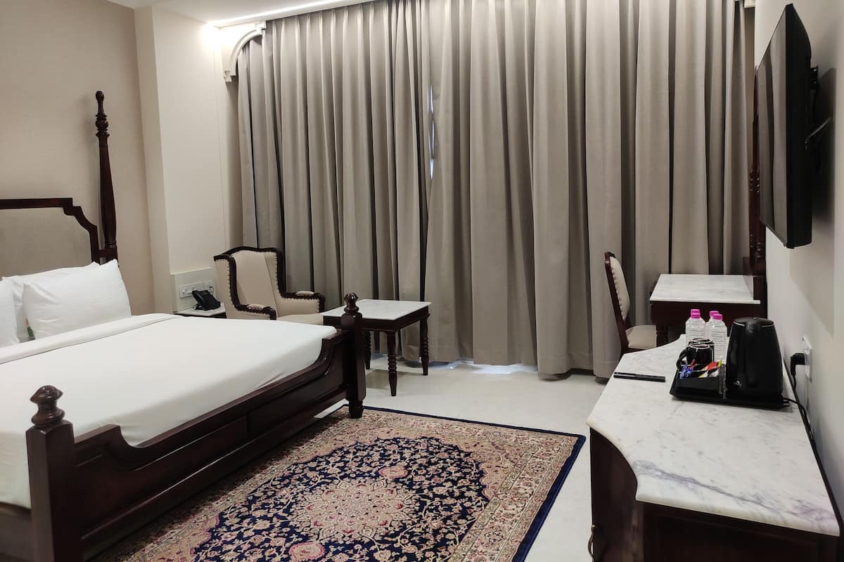 A hotel room with a bed, a chair, a small table, a desk, a TV, and a window with curtains.