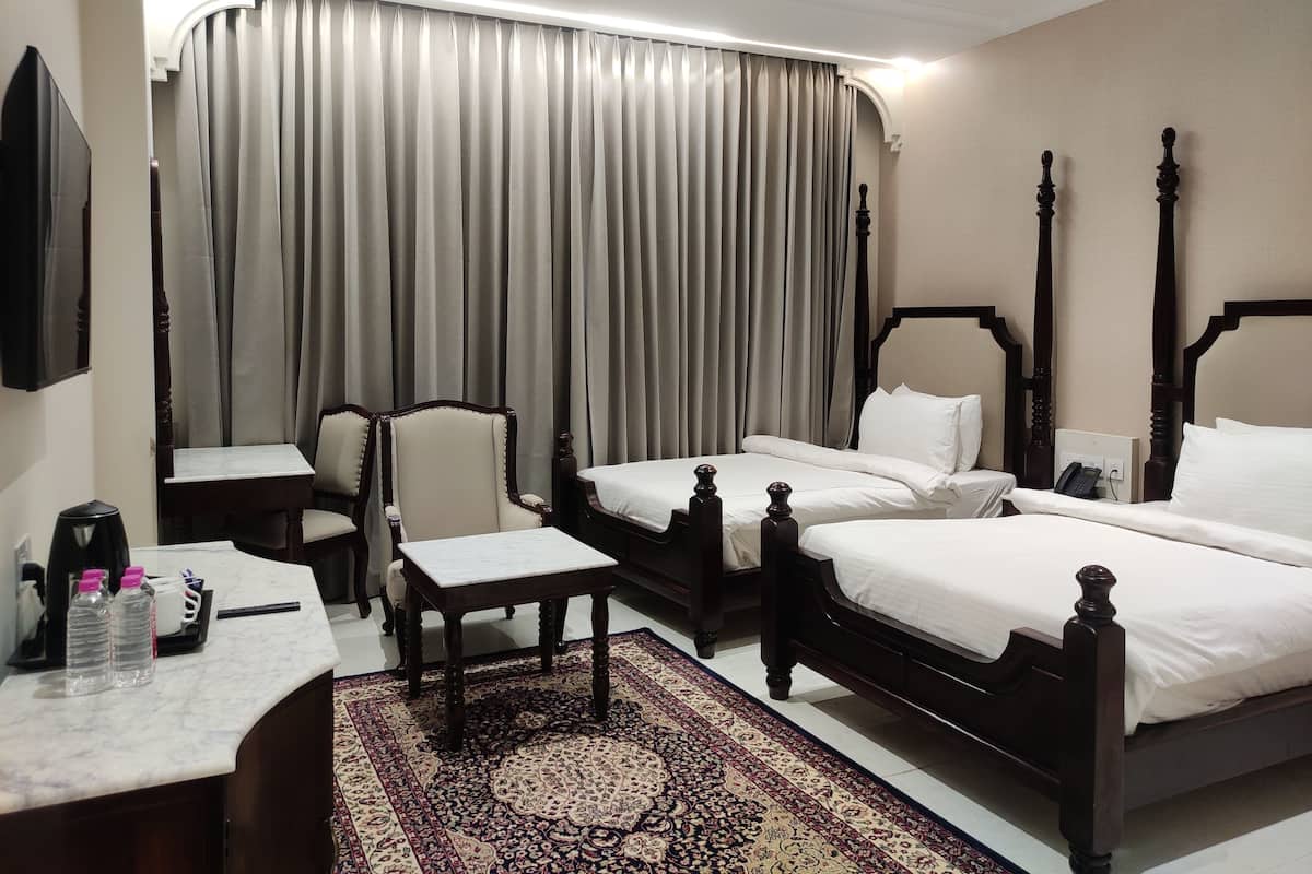 A hotel room with two beds, a desk, a chair, a coffee maker, and a telephone.