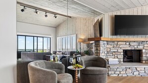 A spacious living room with a stone fireplace, comfortable seating, and a large TV mounted on the wall.