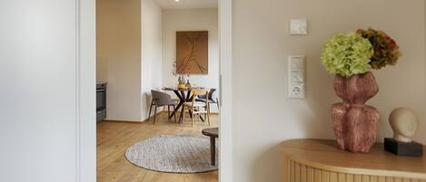 A modern living room with a wooden floor, a round rug, a dining table with chairs, and a vase with flowers on a wooden console table.
