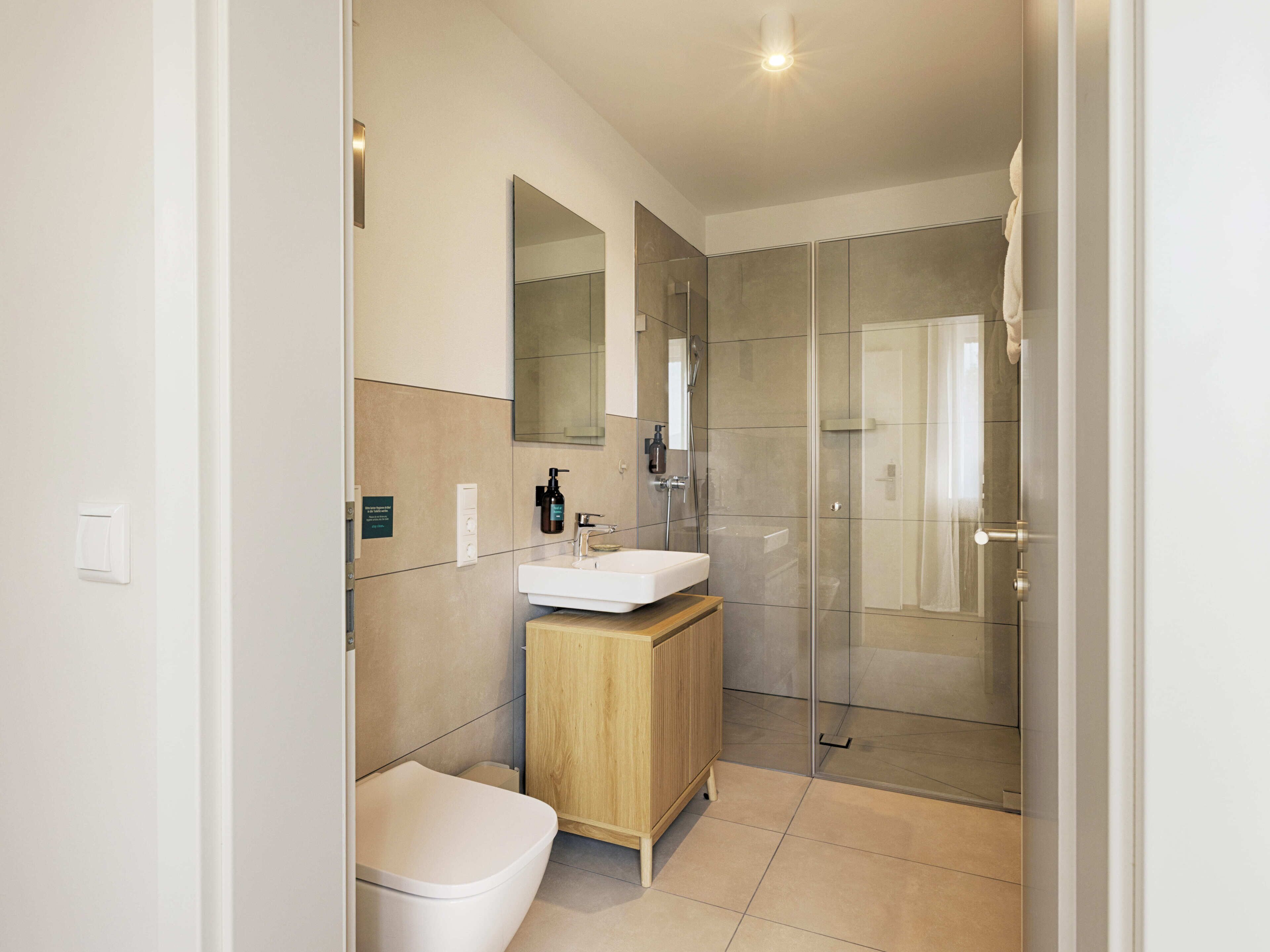 A modern bathroom with a toilet, sink, mirror, and glass shower enclosure.