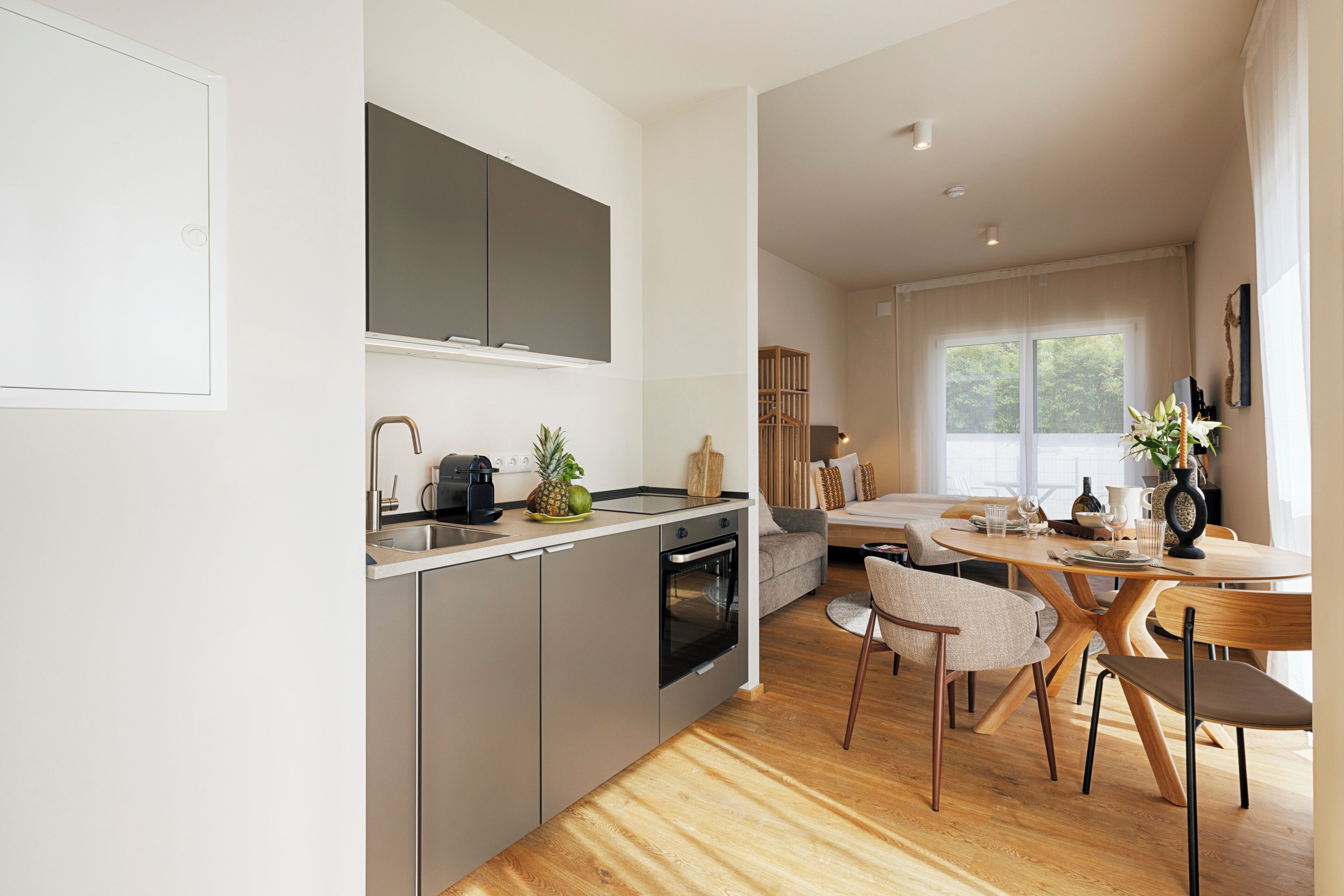 Una cocina moderna con horno empotrado, un comedor con mesa redonda de madera y un sofá.